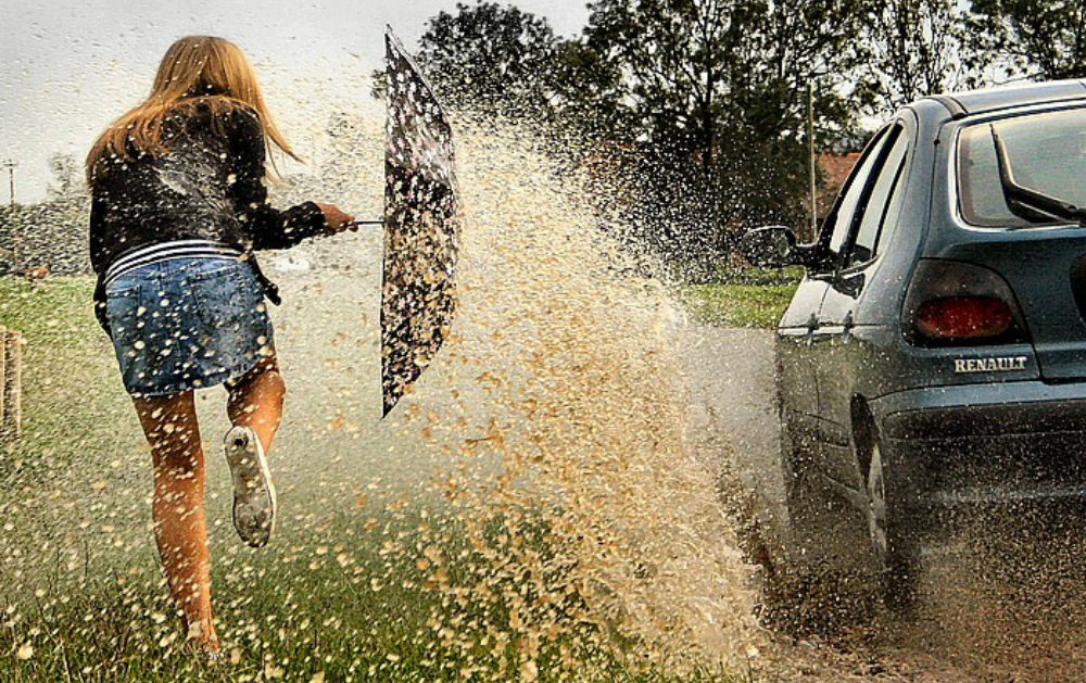 Woman splashed by car going through a puddle